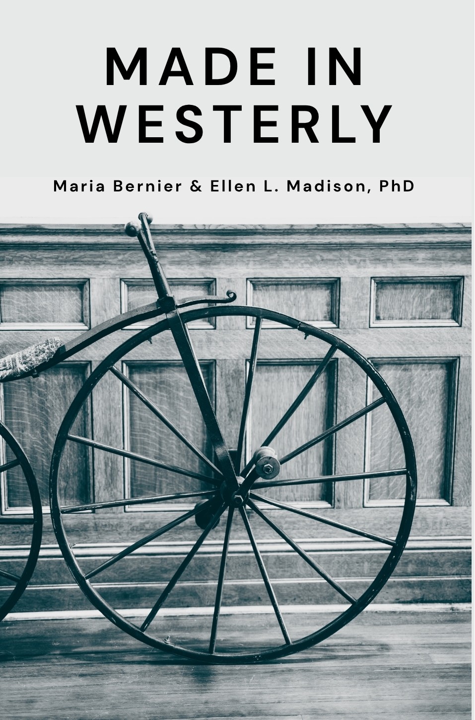 Cover of book Made in Westerly with a black and white photo of the simple front wheel of a velocipede in front of wooden wainscoting.